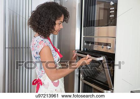 "Mid adult woman in kitchen, using oven" View Large Photo Image Stock Image - "Mid adult woman in kitchen, using oven". Fotosearch