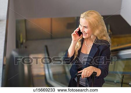 Mid adult woman on esculator using smartphone looking away smiling View Large Photo Image Stock Image - Mid adult woman on esculator using smartphone looking away smiling. Fotosearch