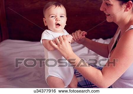 Stock Photograph - Mother and baby boy playing on bed. Fotosearch
