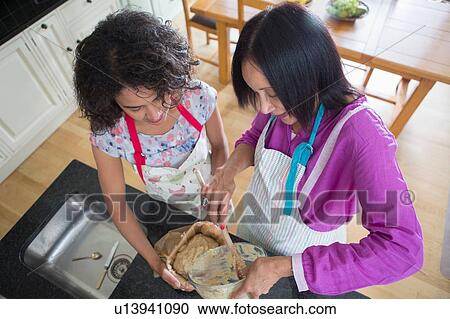 Stock Image - "Mother and grown daughter, cooking in kitchen". Fotosearch
