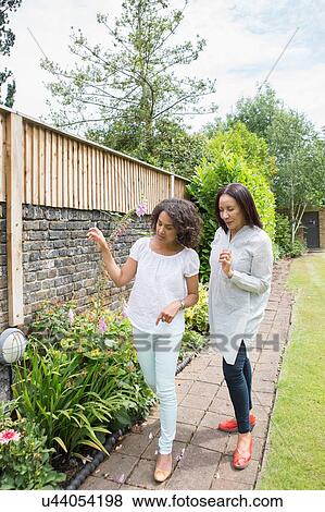 Stock Photo - Mother and grown daughter looking at plants in garden. Fotosearch