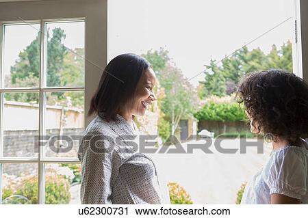 Stock Image - "Mother and grown daughter, standing by patio door, talking". Fotosearch