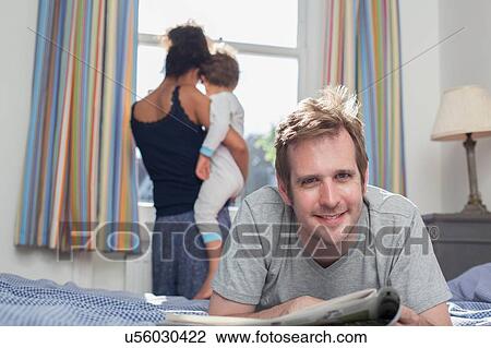 "Mother and son looking out of window, father lying on bed reading newspaper" View Large Photo Image Stock Image - "Mother and son looking out of window, father lying on bed reading newspaper". Fotosearch