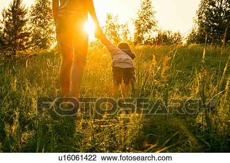 Stock Image - "Mother and son, walking through field at sunset, rear view". Fotosearch