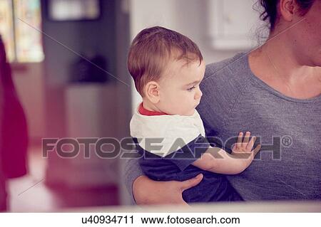Stock Image - Mother carrying baby boy in kitchen. Fotosearch
