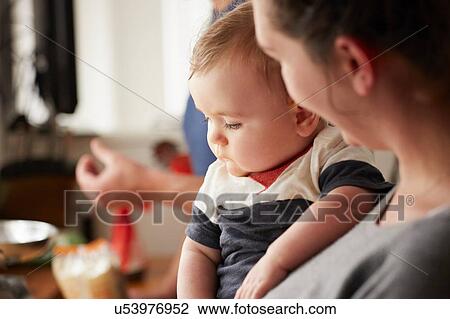 Stock Image - Mother carrying baby boy in kitchen. Fotosearch