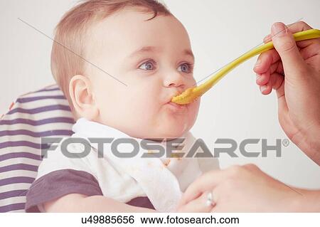 Stock Photograph - Mother feeding baby boy in baby chair. Fotosearch