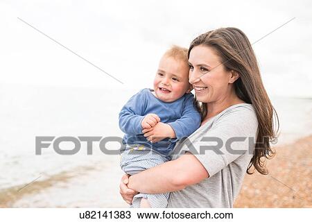 Stock Image - Mother hugging young son on pebble beach. Fotosearch