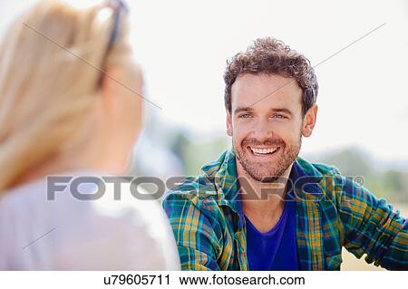 Stock Image - Over shoulder view of mid adult man sitting smiling at young woman. Fotosearch