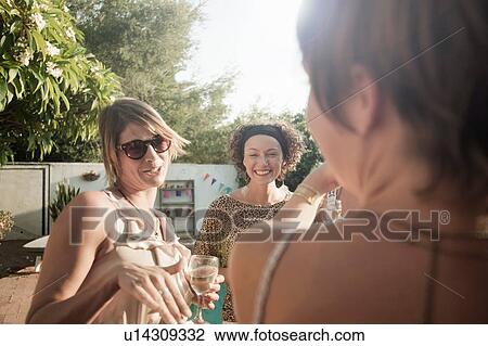 Over shoulder view of small group of friends holding drinks talking and smiling View Large Photo Image Stock Image - Over shoulder view of small group of friends holding drinks talking and smiling. Fotosearch