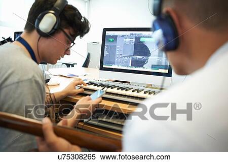 "Over shoulder view of young men wearing headphones using recording equipment, looking down at smartphone" View Large Photo Image Stock Photography - "Over shoulder view of young men wearing headphones using recording equipment, looking down at smartphone". Fotosearch