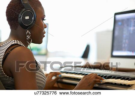 Over shoulder view of young woman wearing headphones playing keyboard View Large Photo Image Stock Photograph - Over shoulder view of young woman wearing headphones playing keyboard. Fotosearch