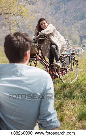 Over the shoulder view of young woman on bicycle chatting to mid adult man View Large Photo Image Stock Image - Over the shoulder view of young woman on bicycle chatting to mid adult man. Fotosearch