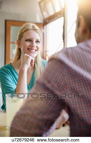Over the shoulder view of young woman sitting with hand on chin looking at young man smiling View Large Photo Image Stock Photograph - Over the shoulder view of young woman sitting with hand on chin looking at young man smiling. Fotosearch