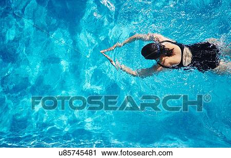Stock Image - Overhead view of mature woman swimming in swimming pool. Fotosearch