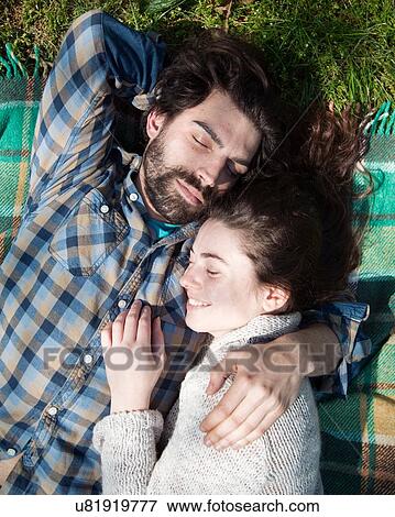 Stock Photo - Overhead view of young couple lying with eyes closed on picnic blanket. Fotosearch