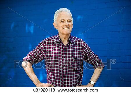Stock Photo - "Portrait of happy senior man, blue brick wall in background". Fotosearch