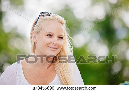 Stock Photograph - Portrait of long haired blonde young woman with sunglasses on head looking away smiling. Fotosearch