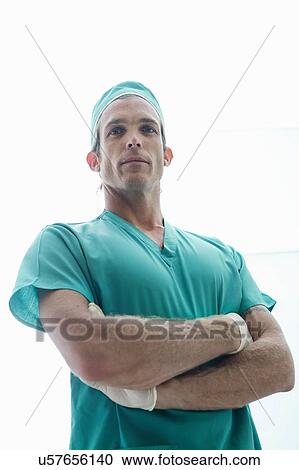 Stock Image - Portrait of male surgeon with arms folded wearing surgical scrubs. Fotosearch