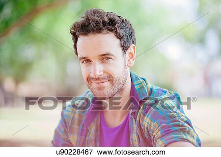 Stock Photo - Portrait of mid adult man wearing checked shirt looking at camera smiling. Fotosearch