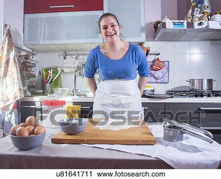 Stock Image - Portrait of mid adult woman preparing food in kitchen. Fotosearch