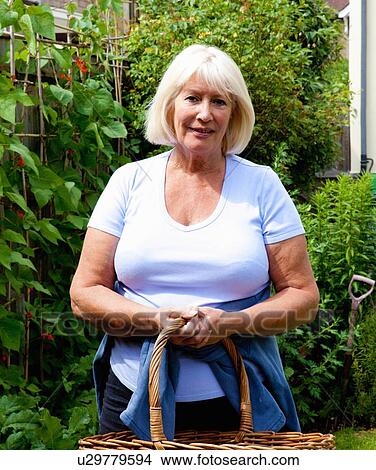 Picture - Portrait of senior woman standing in garden holding wicker basket. Fotosearch