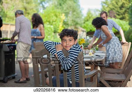 "Portrait of young boy, family preparing food behind him, outdoors" View Large Photo Image Stock Photograph - "Portrait of young boy, family preparing food behind him, outdoors". Fotosearch