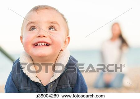 Portrait of young boy on beach with mother sitting behind View Large Photo Image Stock Photo - Portrait of young boy on beach with mother sitting behind. Fotosearch