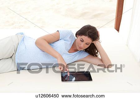 Pregnant mid adult woman lying on beach daybed using digital tablet View Large Photo Image Stock Image - Pregnant mid adult woman lying on beach daybed using digital tablet. Fotosearch