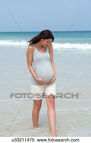 Pregnant mid adult woman paddling in sea with hands on stomach View Large Photo Image Stock Photography - Pregnant mid adult woman paddling in sea with hands on stomach. Fotosearch