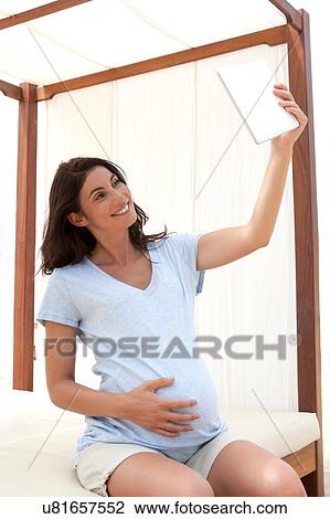Pregnant mid adult woman sitting on daybed taking digital tablet selfie View Large Photo Image Stock Image - Pregnant mid adult woman sitting on daybed taking digital tablet selfie. Fotosearch