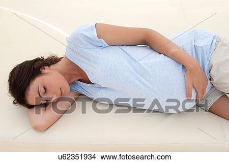 Picture - Pregnant mid adult woman sleeping on daybed with hand on stomach. Fotosearch