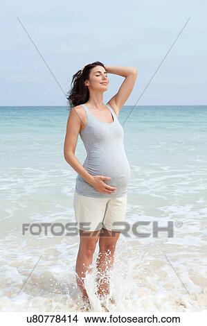 Pregnant mid adult woman standing in sea with eyes closed and hand on stomach View Large Photo Image Picture - Pregnant mid adult woman standing in sea with eyes closed and hand on stomach. Fotosearch