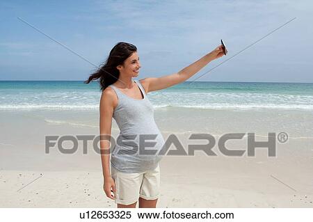 Stock Photography - "Pregnant mid adult woman taking selfie on smartphone at beach, Cape Verde, Africa". Fotosearch