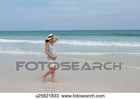 Stock Image - "Pregnant mid adult woman wearing sunhat strolling on beach, Cape Verde, Africa". Fotosearch
