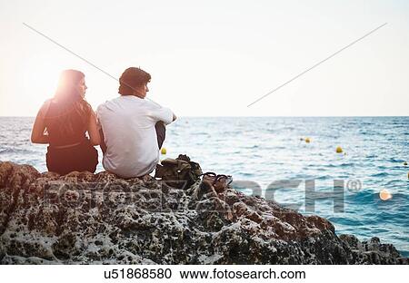 Stock Image - "Rear view of young man and teenage sister on rocky beach, Javea, Spain". Fotosearch