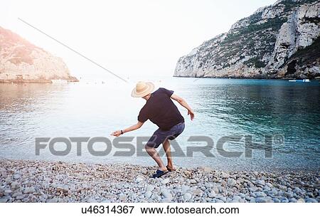 "Rear view of young man skimming stones from beach, Javea, Spain" View Large Photo Image Stock Photo - "Rear view of young man skimming stones from beach, Javea, Spain". Fotosearch