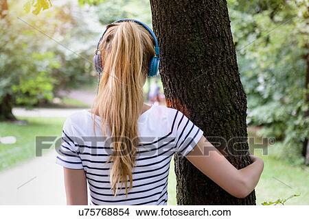 "Rear view of young woman with ponytail, wearing headphones, arm around tree looking away" View Large Photo Image Picture - "Rear view of young woman with ponytail, wearing headphones, arm around tree looking away". Fotosearch