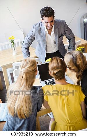 Rear view of young women sitting in front of laptop and young man wearing suit jacket standing smiling View Large Photo Image Stock Image - Rear view of young women sitting in front of laptop and young man wearing suit jacket standing smiling. Fotosearch