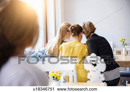 Stock Image - "Rear view of young women sitting side by side, heads together in a huddle". Fotosearch