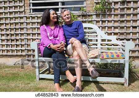 Stock Image - Senior couple sitting on bench in garden. Fotosearch