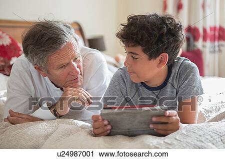 Stock Image - "Senior man and grandson, relaxing on bed, looking at digital tablet". Fotosearch