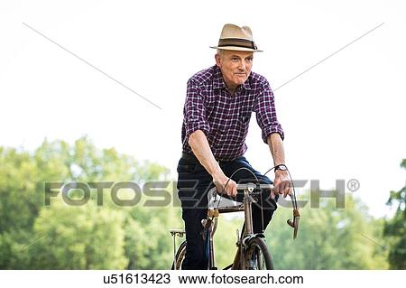 Stock Image - Senior man cycling in park. Fotosearch