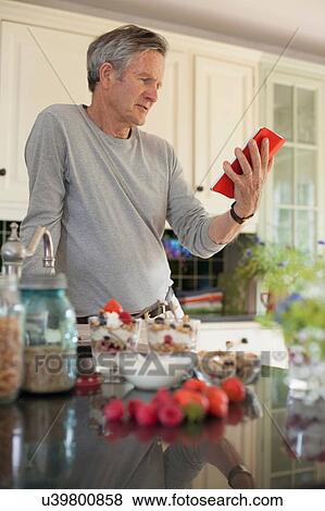 "Senior man in kitchen, looking at digital tablet" View Large Photo Image Stock Photo - "Senior man in kitchen, looking at digital tablet". Fotosearch