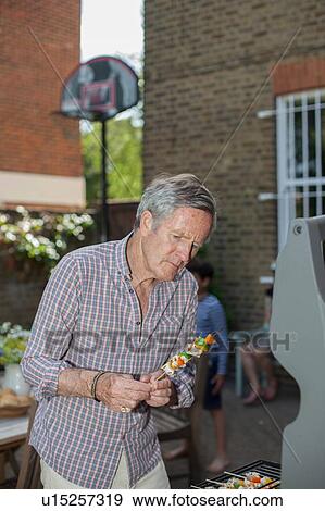 Stock Photo - Senior man placing food on barbecue. Fotosearch