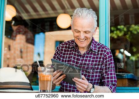 Stock Image - Senior man using digital tablet at cafe. Fotosearch