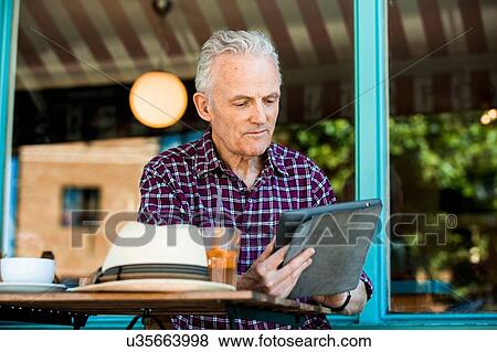 Stock Photo - Senior man using digital tablet at cafe. Fotosearch
