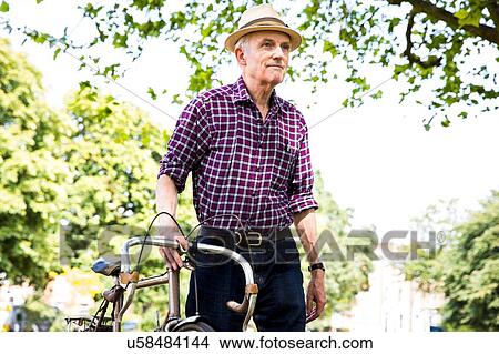 Picture - "Senior man with bicycle in park, Hackney, London". Fotosearch