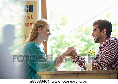 "Side view of couple holding hands across table, looking at each other smiling" View Large Photo Image Stock Image - "Side view of couple holding hands across table, looking at each other smiling". Fotosearch