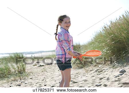 Stock Image - Side view of girl holding orange sports bat looking at camera smiling. Fotosearch